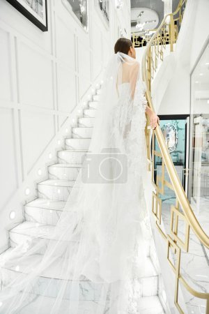 A young brunette bride in a wedding dress stands elegantly on a staircase