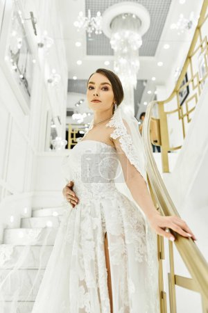 Téléchargez les photos : Jeune mariée brune dans une robe de mariée se tient gracieusement sur un escalier - en image libre de droit