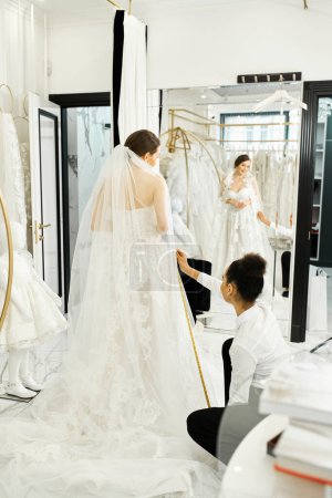 A young bride in a white wedding gown converses with an African American shopping assistant in a luxurious bridal salon.