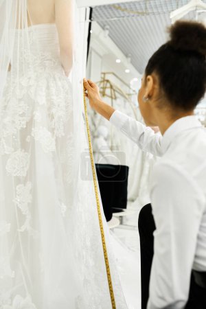 Eine junge Braut misst ein Brautkleid an einer Schaufensterpuppe mit Hilfe einer afroamerikanischen Shopping-Assistentin in einem Brautsalon.