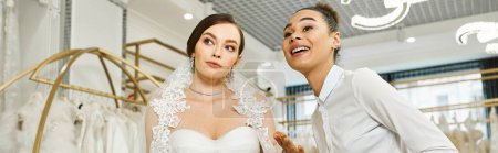 Una joven novia morena en un vestido de novia está acompañada por un asistente de compras afroamericano en un salón de novias.