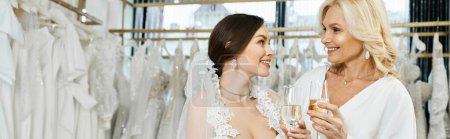 Una joven novia en un vestido de novia está junto a su madre de mediana edad en un salón de novias, compartiendo un momento especial.