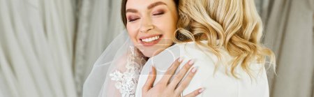 Photo for A young brunette bride in a wedding dress embraces her middle-aged mother in a touching moment in a bridal salon. - Royalty Free Image