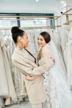 Foto de Una joven novia y su dama de honor abrazándose en un salón de novias. - Imagen libre de derechos