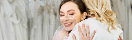 Photo for A young bride in a wedding dress embraces her middle-aged mother in front of a curtain at a bridal salon. - Royalty Free Image