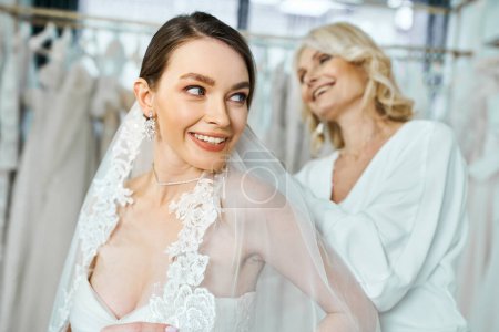 Eine junge brünette Braut im Brautkleid steht neben ihrer Mutter mittleren Alters
