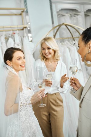 Photo for Three women - a young bride, her middle-aged mother, and a bridesmaid - stand side by side, each holding a champagne glass. - Royalty Free Image