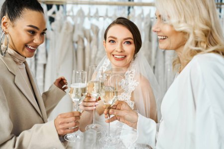 Eine junge brünette Braut im Hochzeitskleid, ihre Mutter mittleren Alters und ihre beste Freundin als Brautjungfer mit Weingläsern im Brautsalon.
