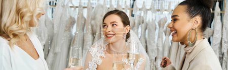 Photo for A young brunette bride in a wedding dress, her middle-aged mother, and her best friend as a bridesmaid standing together in a bridal salon. - Royalty Free Image