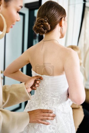 A woman assists a young bride in a white wedding dress in a wedding salon.