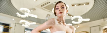 Photo for A stunning brunette bride in a chic white dress stands poised in a glamorous wedding salon. - Royalty Free Image