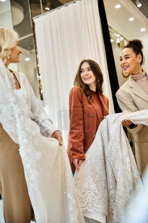 A radiant young bride, her mother, and best friend standing together, shopping for her wedding.