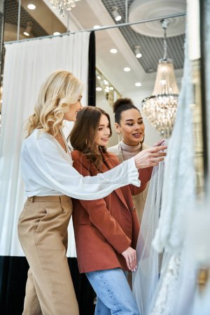Photo for Young beautiful bride shops for her wedding dress with her mother and best friend in a store. - Royalty Free Image