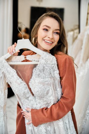 A young woman holds up a dress in a store immersed in the joy of wedding shopping.