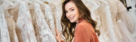 A young bride stands before a selection of wedding dresses, trying to find the perfect gown for her special day.