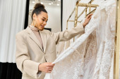 A young beautiful bride carefully examines a wedding dress on a rack t-shirt #698530298
