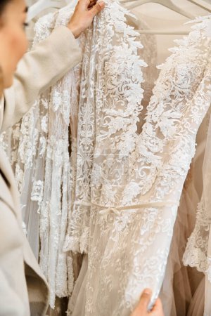 A young bride, carefully examines a dress on a rack in a bridal boutique.