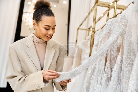 Eine junge schöne Braut blickt auf ein Hochzeitskleid auf einem Gestell und lächelt, als sie eines ansieht.