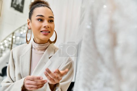 A young bride shops for her wedding dress, standing in front of a mirror and gowns