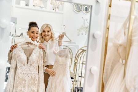 Two women, a young bride and a shop assistant, stand in front of a mirror assessing wedding attire.