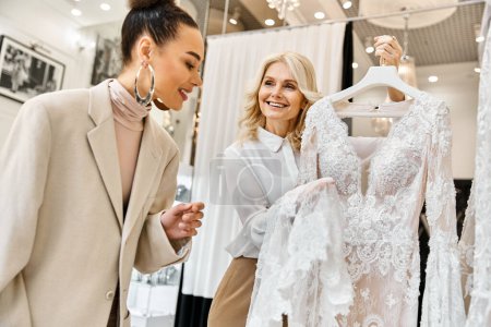 Zwei Frauen, eine junge schöne Braut und eine Verkäuferin, stöbern in eleganten Kleidern in einem Geschäft.