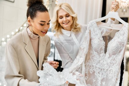 Two women admiring a white gown on a hanger in a bridal shop. The bride-to-be and shop assistant are discussing the dress.
