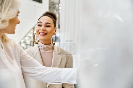 Photo for Two women dressed elegantly stand together looking at each other, possibly shopping for a wedding attire. - Royalty Free Image