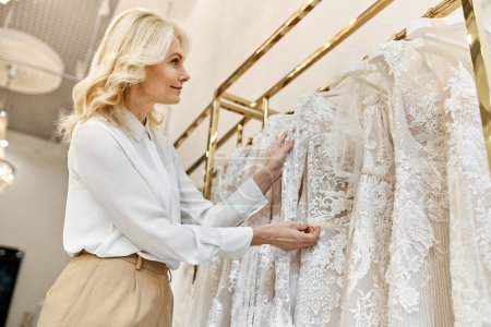 Un hermoso asistente de compras de mediana edad ayuda a una mujer a navegar a través de vestidos de novia en un estante en un salón de novias.