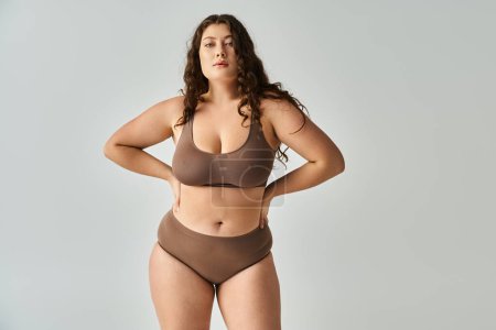 Photo for Attractive plus size young woman in underwear with brown hair posing with hands on grey background - Royalty Free Image