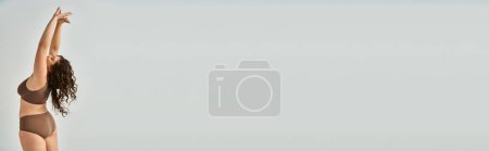 Téléchargez les photos : Bannière de jolie jeune femme courbée en sous-vêtements avec les cheveux bruns bouclés du dos mettant les mains vers le haut - en image libre de droit