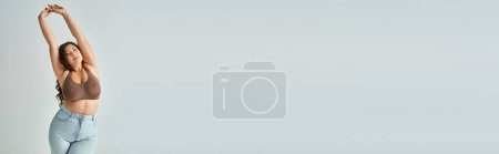 Téléchargez les photos : Bannière de femme courbée gaie en soutien-gorge marron et jean bleu avec cheveux bouclés mettant les mains à - en image libre de droit
