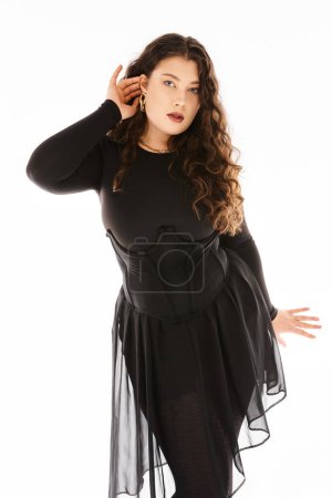 Téléchargez les photos : Belle jeune femme courbée en tenue élégante noire avec des cheveux bouclés montrant sa boucle d'oreille - en image libre de droit