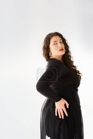 Téléchargez les photos : Séduisante femme plus taille en tenue élégante noire avec des cheveux bouclés posant du dos avec la main sur la hanche - en image libre de droit