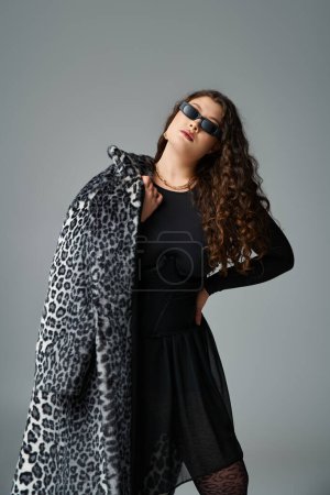 beautiful curvy woman in sunglasses posing with fur coat over shoulder and hand on waist