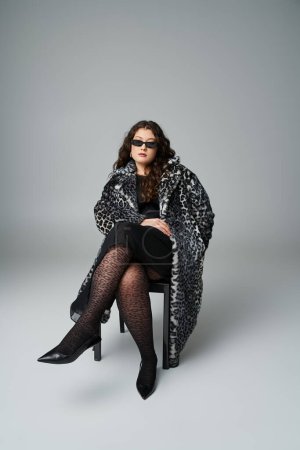 seductive plus size woman in leopard fur coat and sunglasses sitting on black chair with cross legs