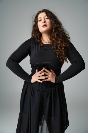 attractive plus size girl looking to camera with hands on waist on grey background
