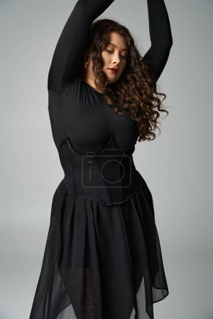 alluring plus size woman putting arms to up and looking to down on grey background