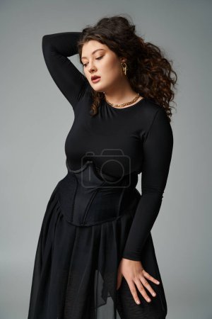 alluring plus size girl in black stylish outfit putting hand behind head and looking down
