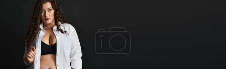 Téléchargez les photos : Bannière de femme taille plus en chemise blanche, soutien-gorge noir et pantalon avec cheveux bouclés sur fond sombre - en image libre de droit