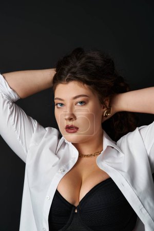 portrait of charming curvy woman in shirt and bra putting hands behind head and holding hair