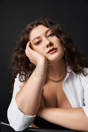 portrait of charming plus size girl in her 20s leaning on hand and looking to camera