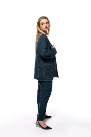 attractive woman with blonde hair in blue elegant blazer posing on white background and looking away