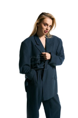appealing woman with blonde hair in stylish blazer posing on white backdrop and looking at camera