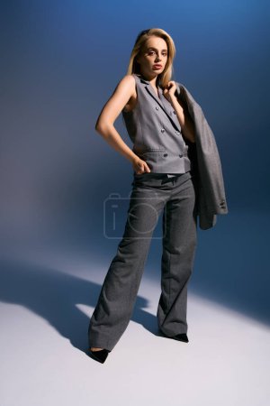 elegant woman in silver chic vest and suit posing on dark blue backdrop and looking at camera