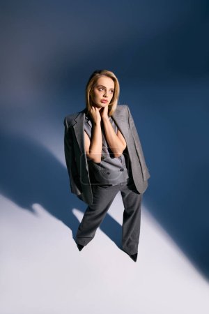 attractive elegant woman with blonde hair in debonair vest and suit looking away on blue backdrop