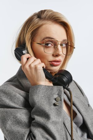 mujer elegante de buen aspecto con gafas en traje debonair hablando por teléfono y mirando a la cámara