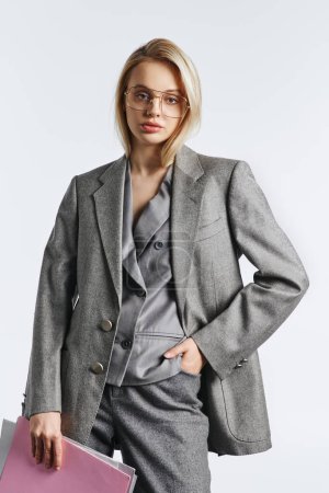 Foto de Hermosa mujer con gafas con estilo en traje elegante gris posando con papeleo y mirando a la cámara - Imagen libre de derechos