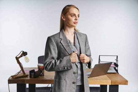 Foto de Debonair mujer de negocios guapa en traje gris sofisticado con cabello rubio mirando hacia otro lado - Imagen libre de derechos
