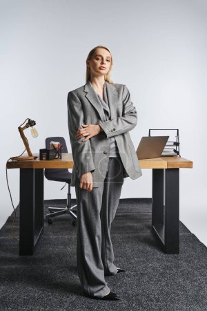 Foto de Atractiva mujer de negocios trabajadora en traje gris sofisticado mirando a la cámara en el fondo gris - Imagen libre de derechos