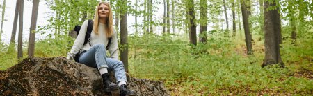 Smiling pretty blonde woman hiker sitting on a rock in forest and looking away, banner